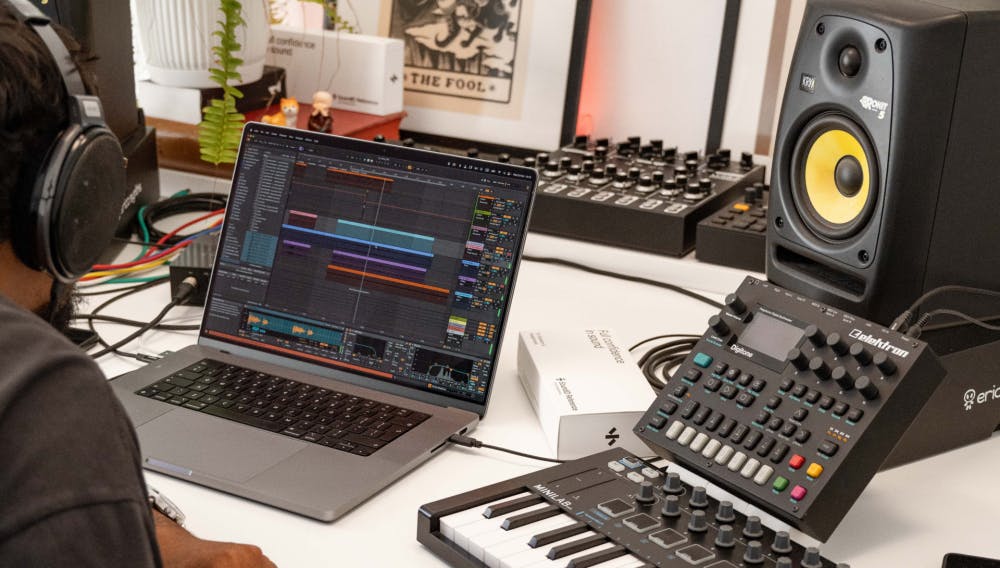 Music producer using SoundID VoiceAI in Ableton Live with KRK monitors, MIDI controller, and Elektron Digitone synth on a white studio desk