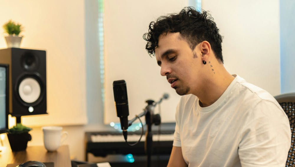 Male vocal engineer recording in a home studio setup with studio monitors, microphone, and keyboard