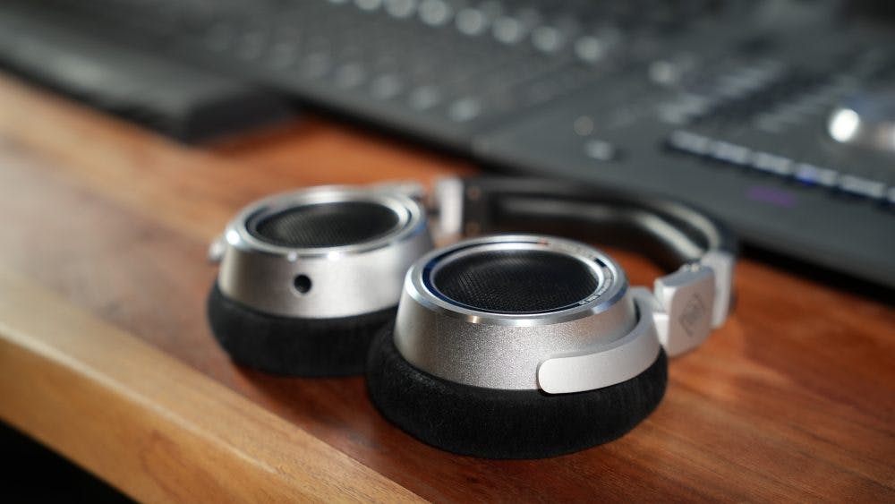 Neumann NDH 30 headphones folded flat showing aluminum construction and mesh grilles on studio desk