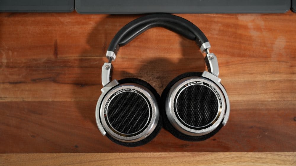 Neumann NDH 30 headphones flat on wooden surface showing mesh grilles and aluminum construction detail