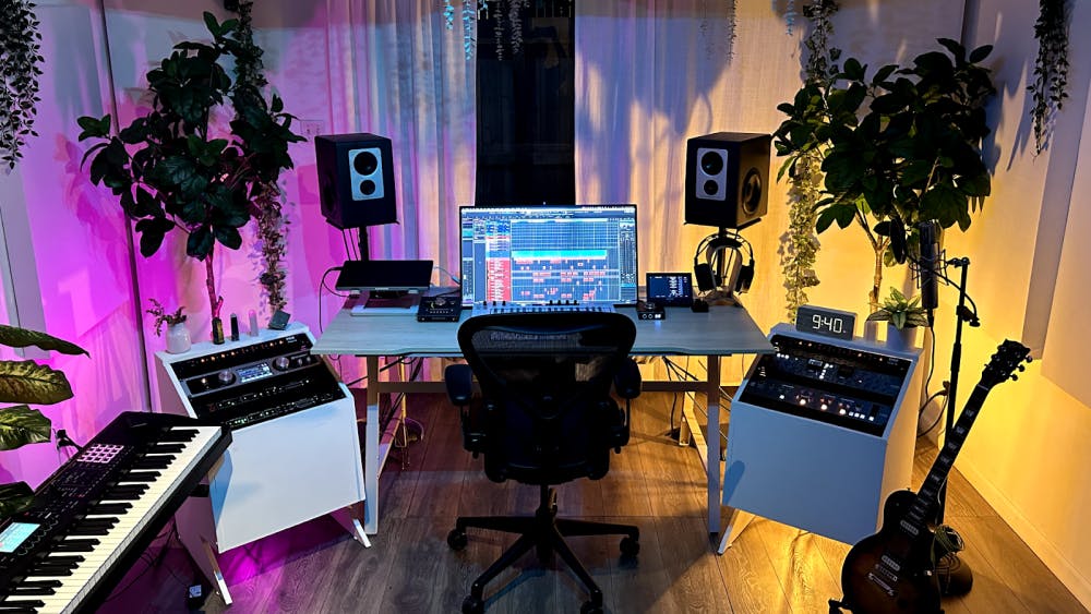 A stylish home recording studio interior featuring music plaques and album awards on the wall, a wooden shelf with signed albums and small plants, and leafy potted plants placed throughout for a cozy, organic atmosphere.