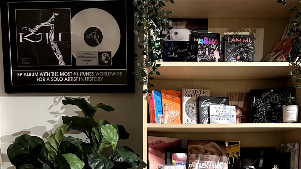 A stylish home recording studio interior featuring music plaques and album awards on the wall, a wooden shelf with signed albums and small plants, and leafy potted plants placed throughout for a cozy, organic atmosphere.