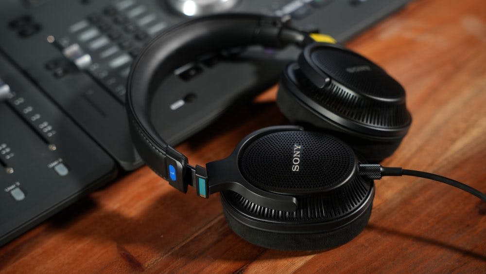 Sony MDR-MV1 headphones on wooden desk with studio mixing equipment background